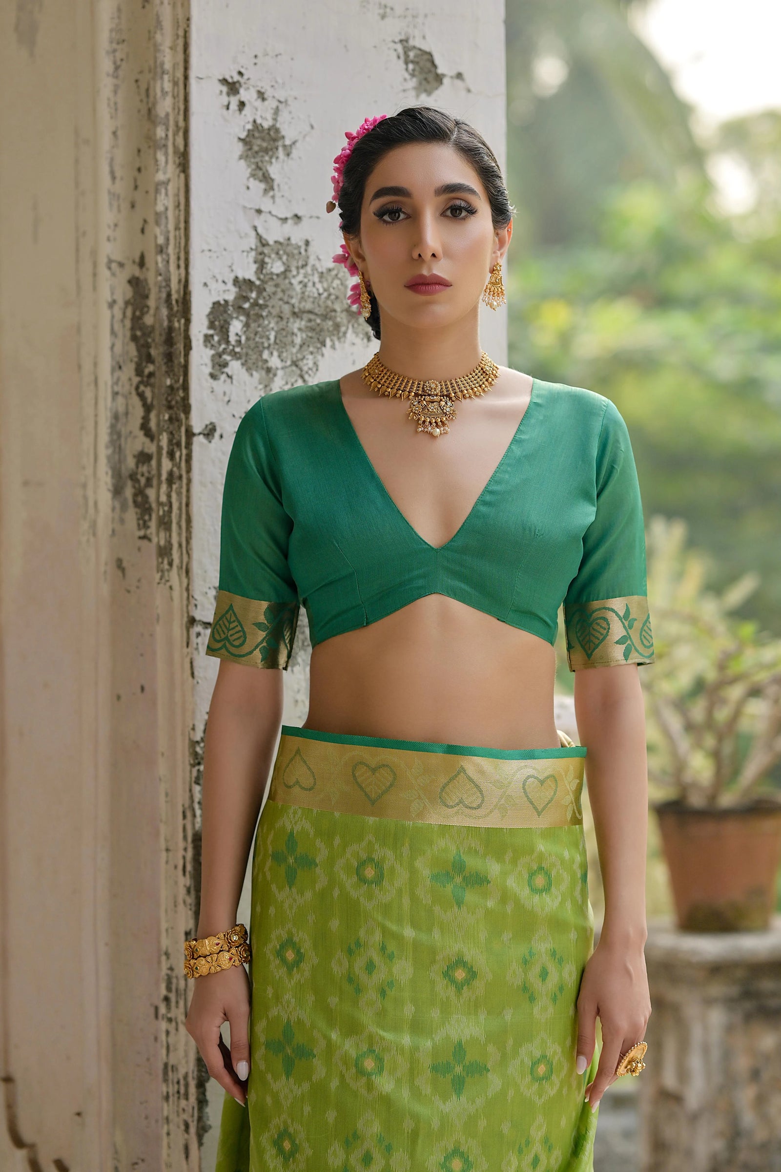 Woman wearing a green traditional outfit with a patterned skirt, standing outdoors.
