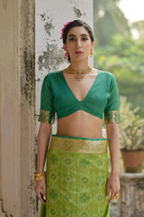 Woman wearing a green traditional outfit with a patterned skirt, standing outdoors.