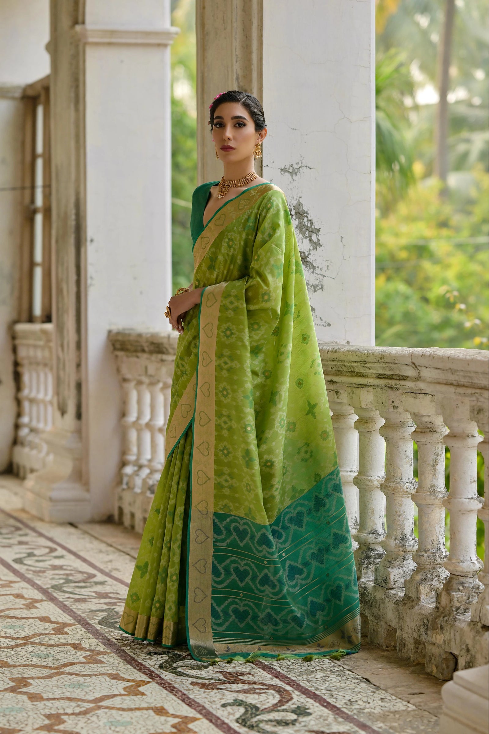 Woman in a green saree standing on a balcony with a garden view