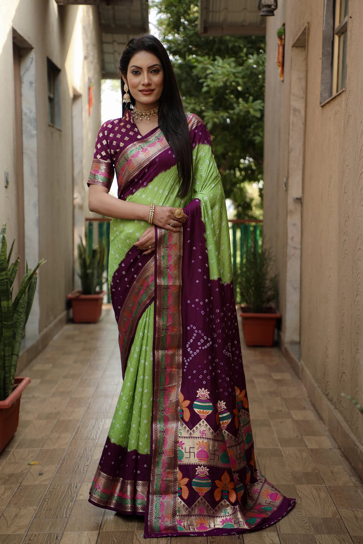 Woman wearing a green and purple saree with a patterned border in an outdoor setting.