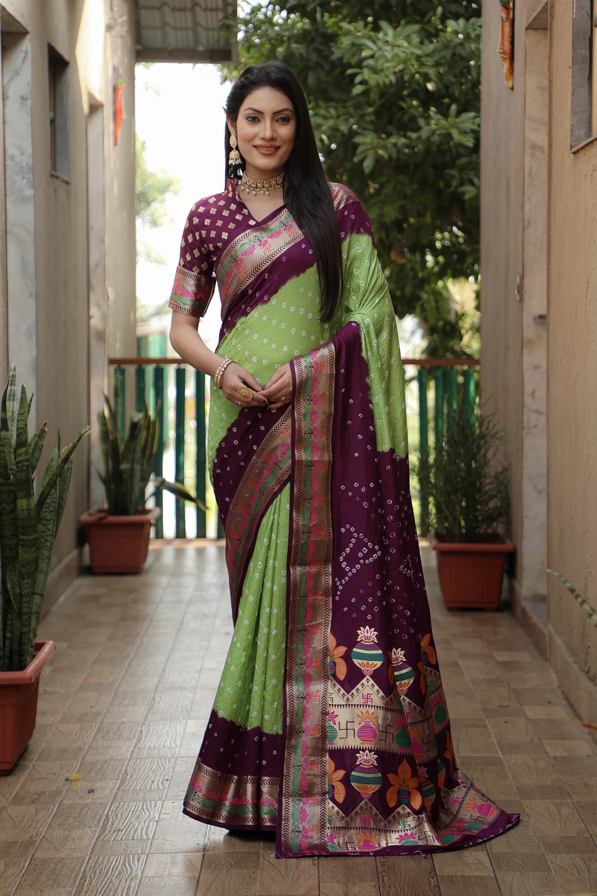Woman wearing a green and purple saree standing in an outdoor setting.