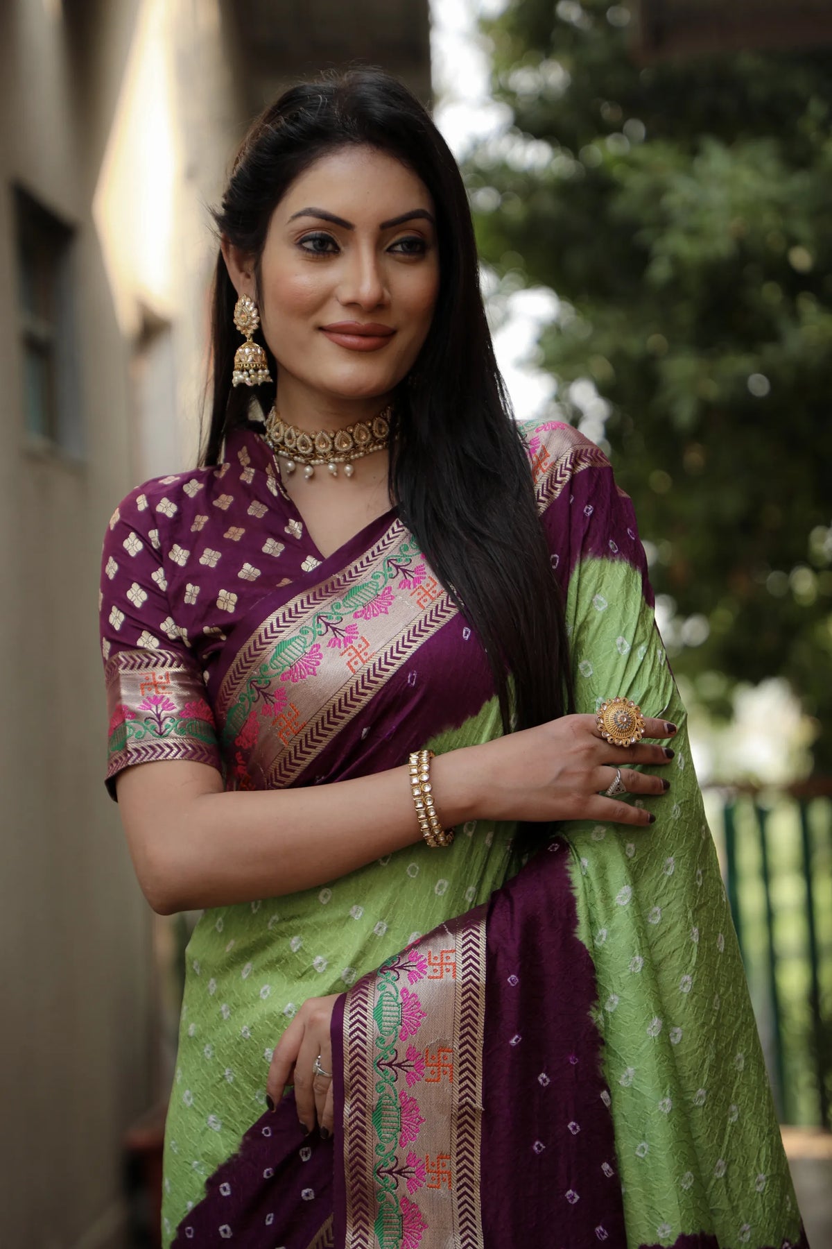Woman wearing a green and purple saree with jewelry outdoors
