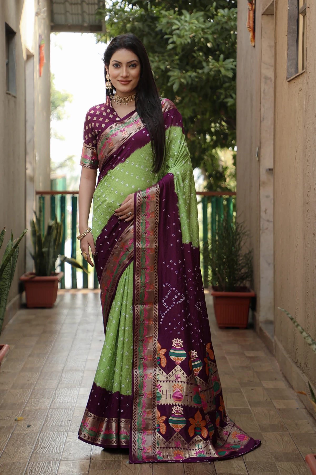 Woman wearing a green and purple saree with a patterned border in an outdoor setting.