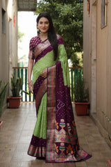 Woman wearing a green and purple saree with a patterned border in an outdoor setting.