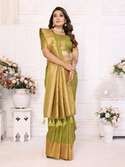 Woman in a green saree standing in a decorated room with flowers and white furniture.