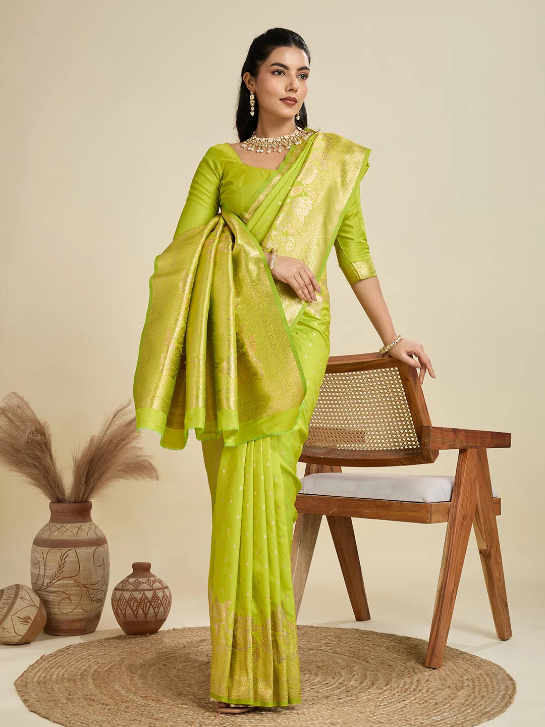 Woman in a green saree standing next to a wooden chair with decorative elements.