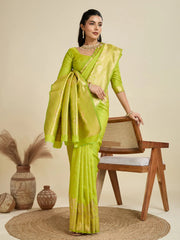 Woman in a green saree standing next to a wooden chair with decorative elements.