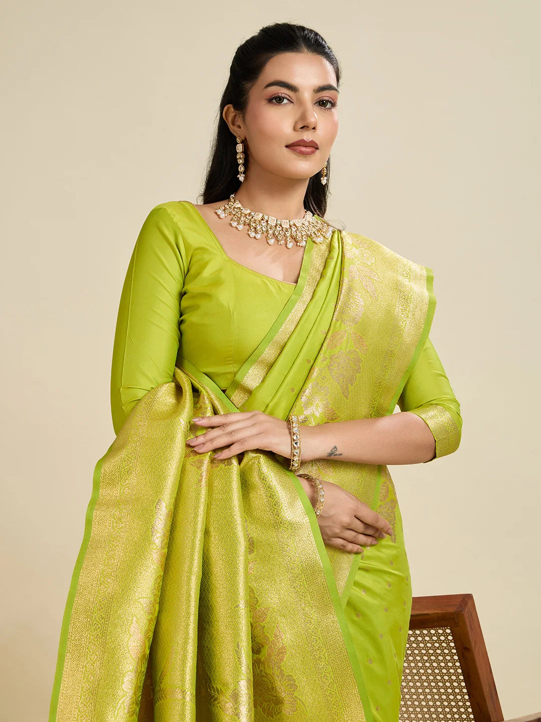 Woman wearing a green saree with a matching blouse against a beige background