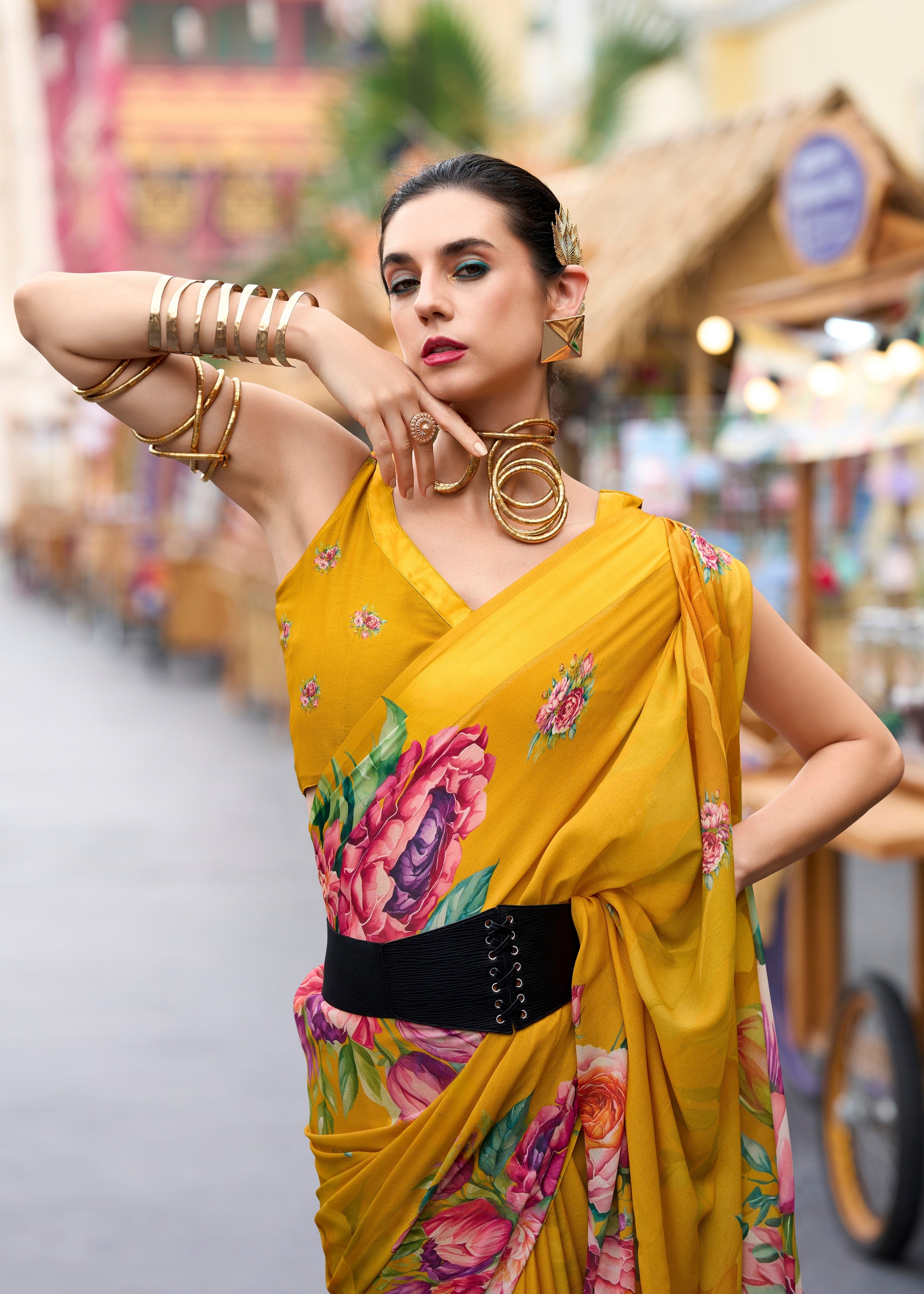 Woman in a yellow saree with floral patterns posing outdoors.