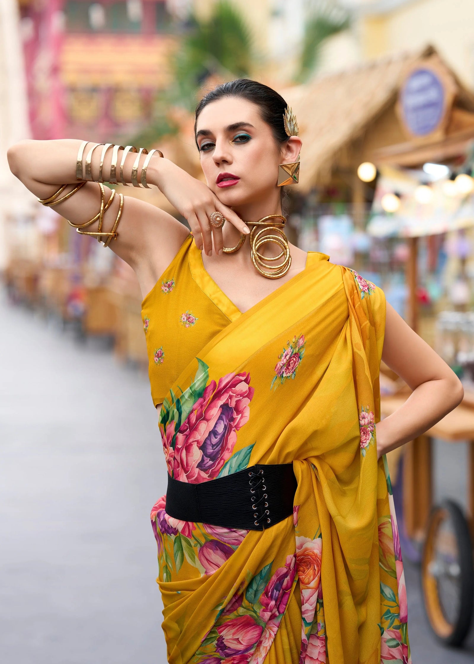 Woman in a yellow saree with floral patterns posing outdoors.