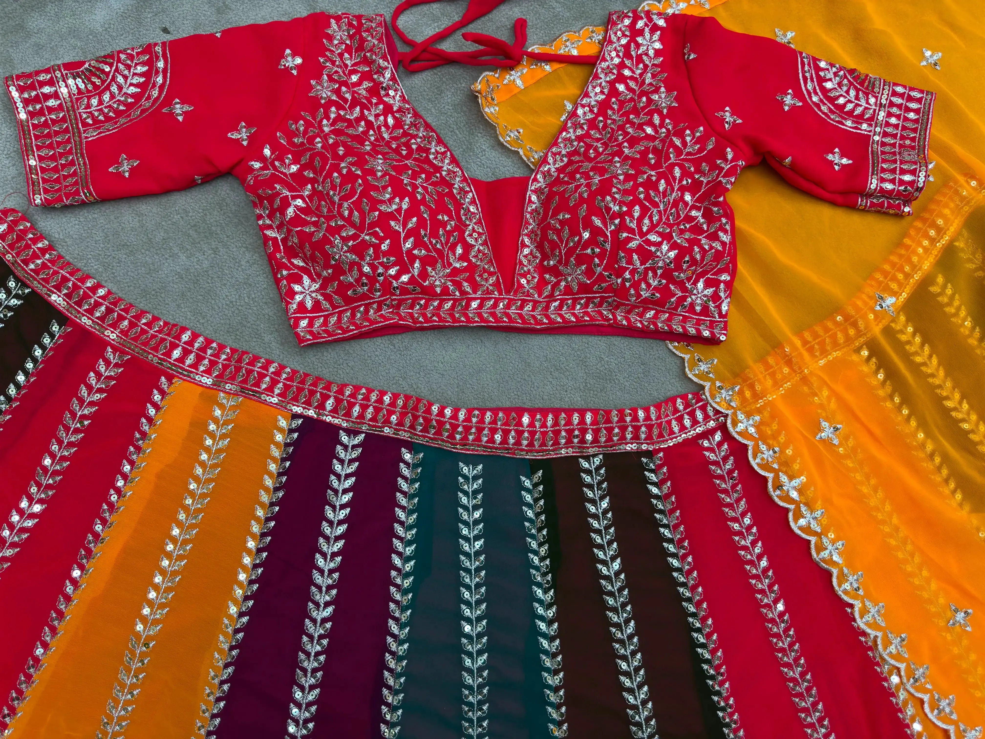 Flat lay of multicolor lehenga set showing red embroidered choli and orange dupatta with sequins border