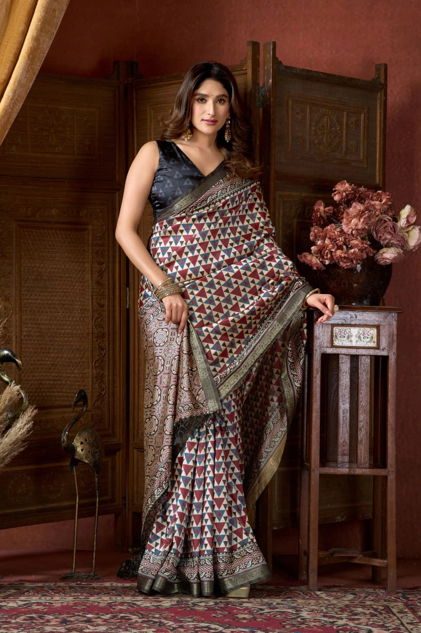 Woman in a patterned saree standing in an elegant room with wooden furniture and decorative elements.