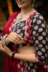 Woman wearing a traditional patterned blouse with a red saree, close-up of hands.