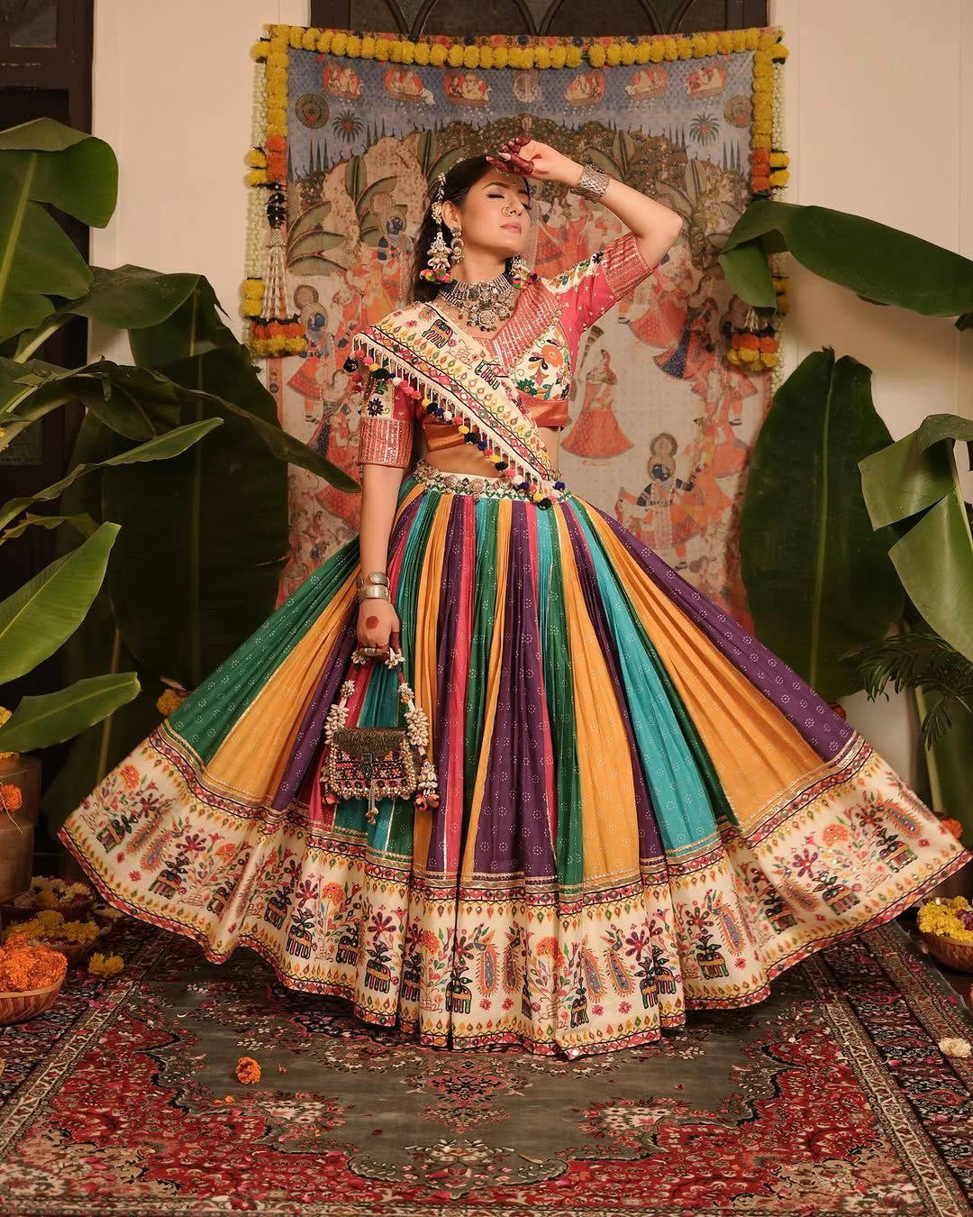 Woman in a colorful traditional outfit standing in front of a decorative wall with plants around.