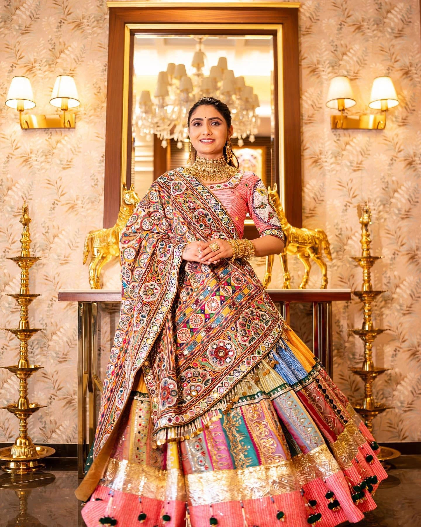 Woman in a colorful traditional outfit standing in a decorated room with mirrors and lights.