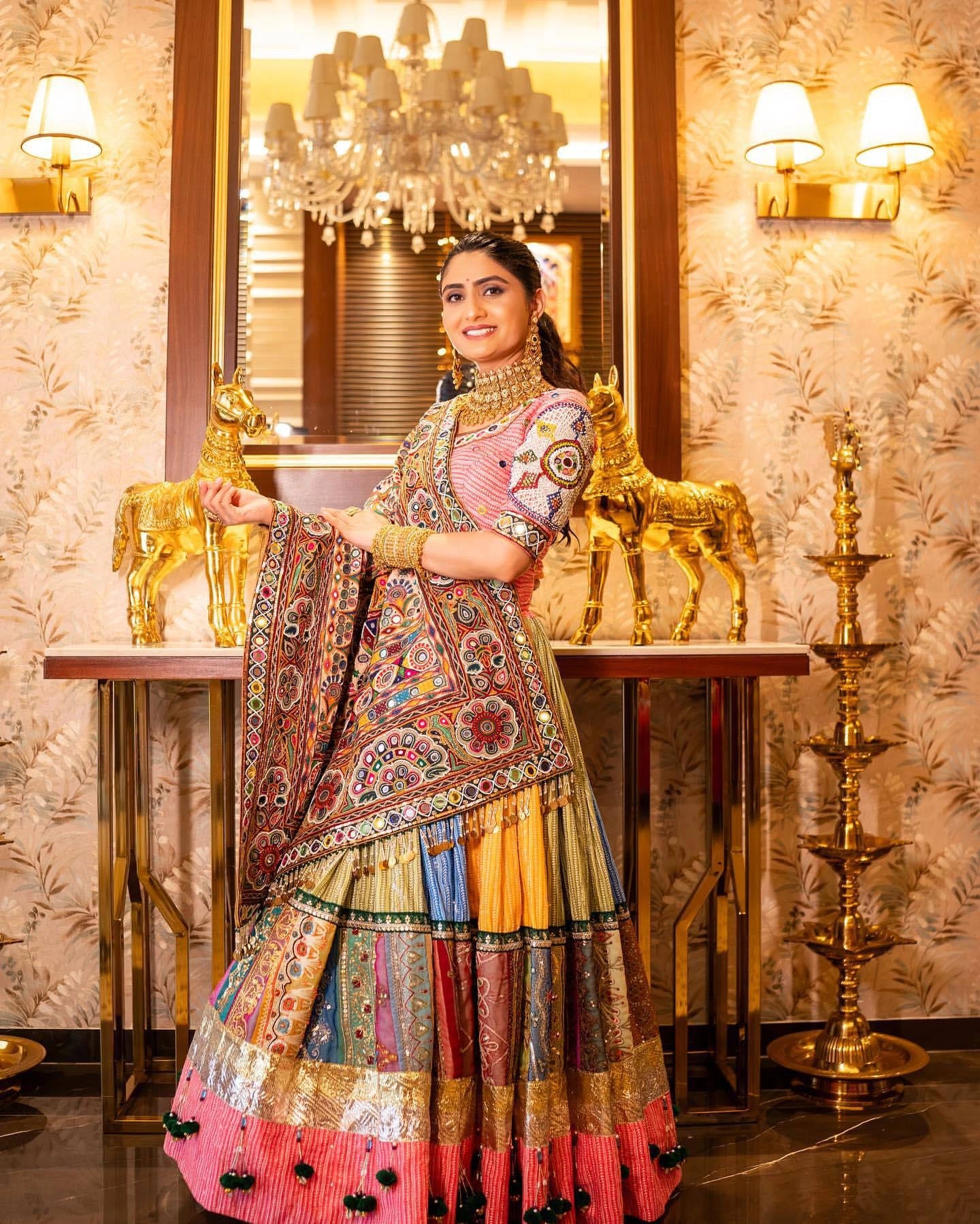 Woman in a colorful traditional outfit standing in an ornate room with chandeliers.