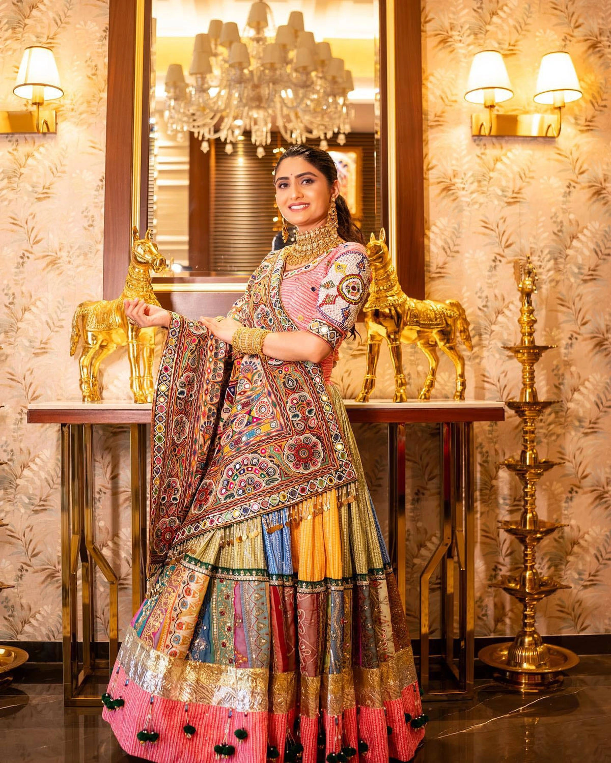 Woman in a colorful traditional outfit standing in an ornate room with chandeliers.