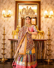 Woman in traditional multicolored outfit standing in a decorated room with chandelier and wall lights.