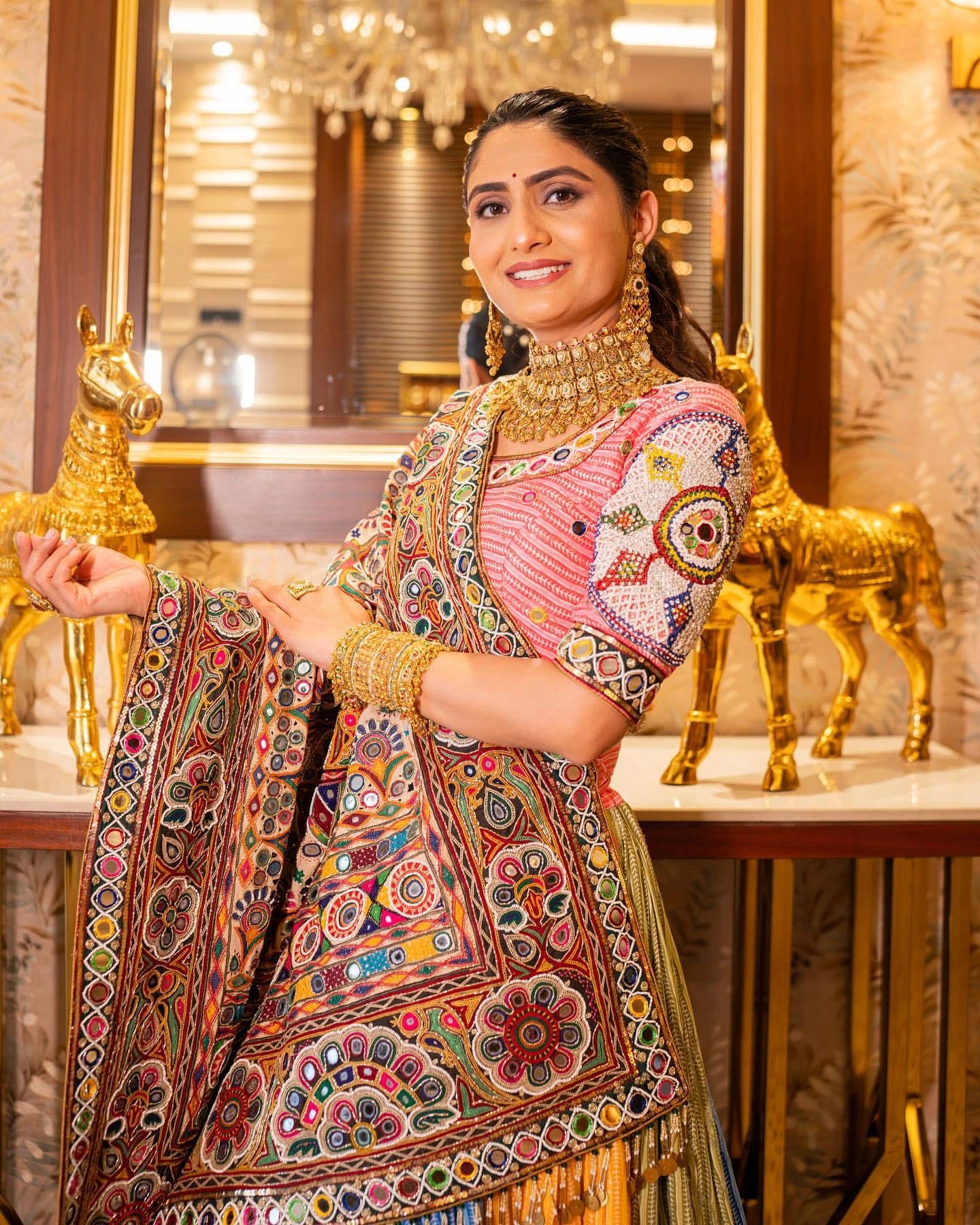 Woman in traditional embroidered outfit with gold jewelry in a decorated interior setting