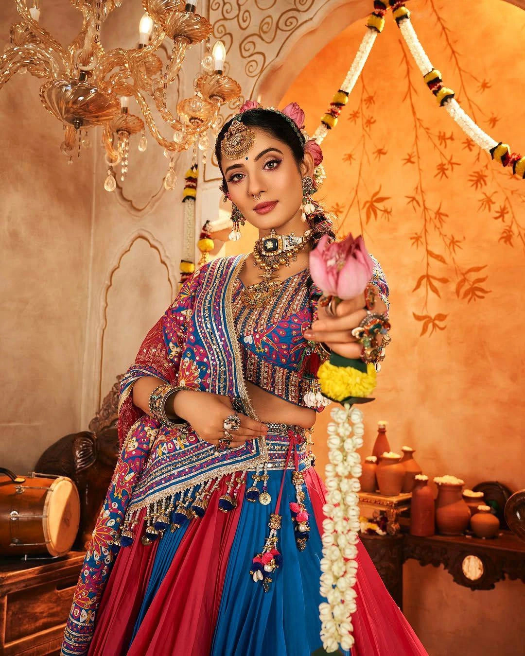 Woman in traditional attire holding a pink flower in an ornate room.