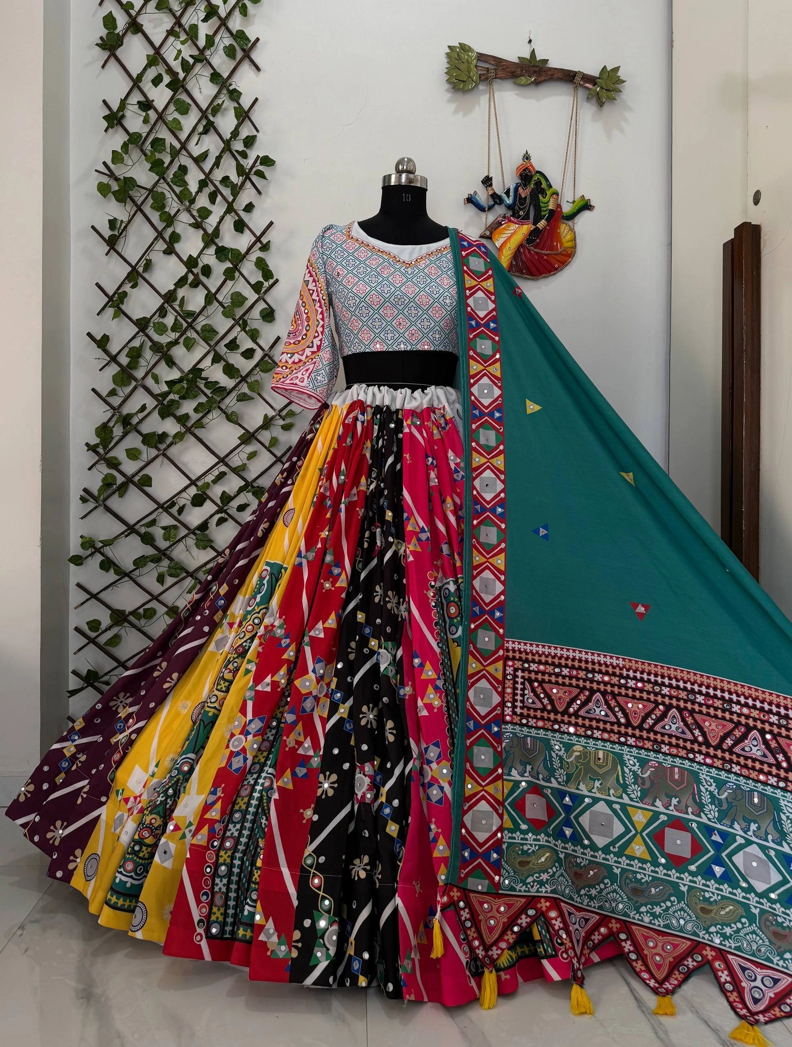 Colorful traditional outfit with a patterned dupatta on a mannequin against a decorative wall.