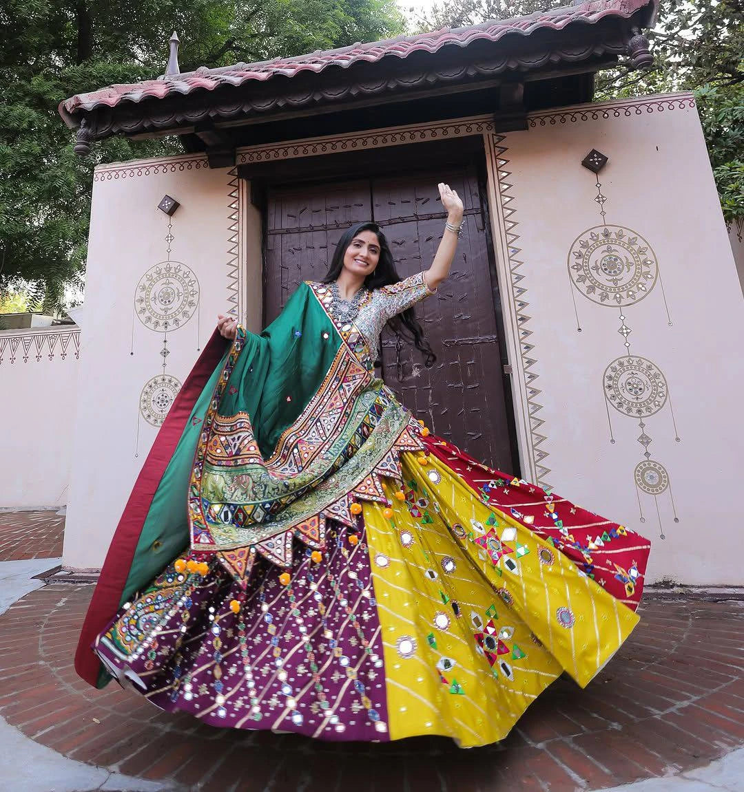 Woman in a colorful traditional outfit standing in front of a decorative building entrance.