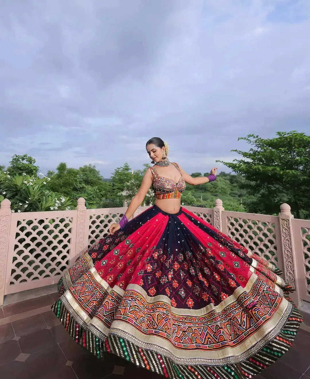 Woman in traditional multicolored lehenga dancing outdoors with trees and sky in the background