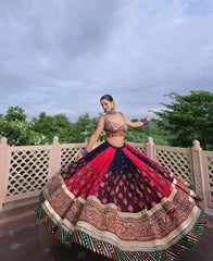 Woman in traditional multicolored lehenga dancing outdoors with trees and sky in the background