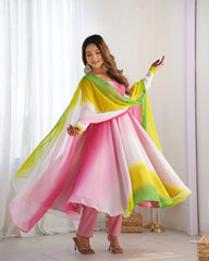 Woman in a colorful traditional outfit standing in a bright room with white curtains.