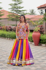 Woman in a colorful traditional outfit standing outdoors with greenery and a building in the background
