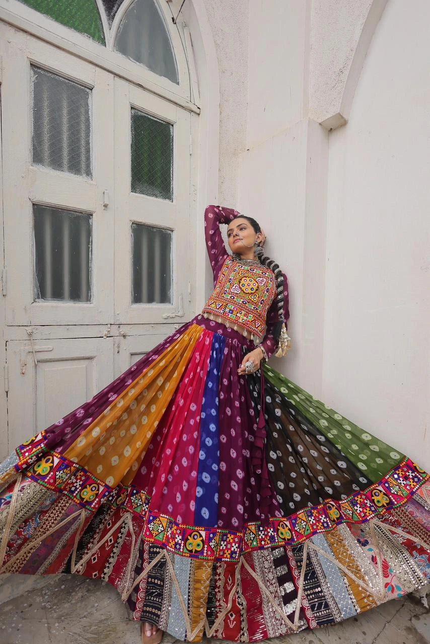 Woman in a colorful traditional outfit standing in front of a white wall with a window.