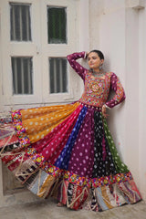 Woman in a colorful traditional outfit standing against a white wall.
