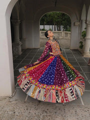 Woman in a colorful traditional outfit sitting on a stone floor with an archway in the background.