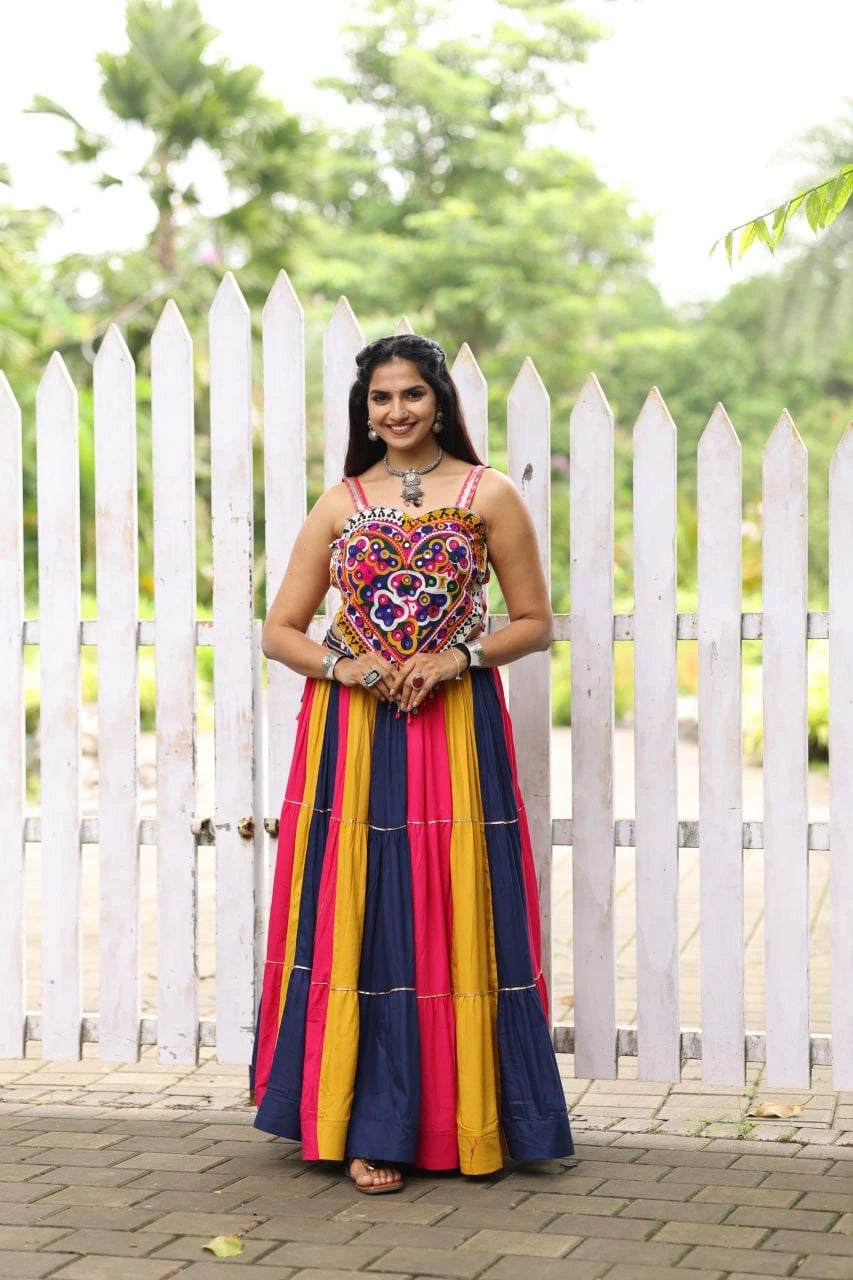 Woman in a colorful traditional outfit standing in front of a white picket fence.