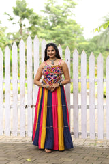 Woman in a colorful traditional outfit standing in front of a white picket fence.