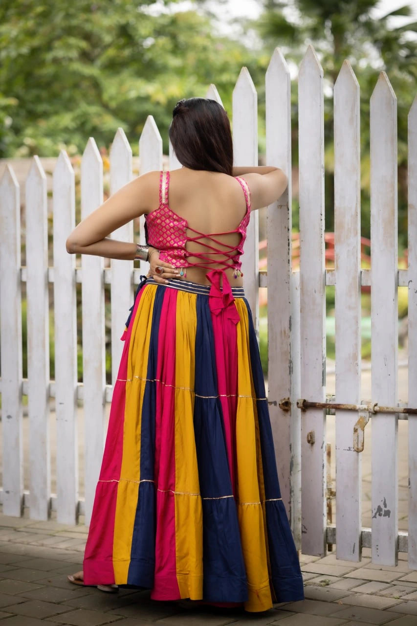 Woman wearing a colorful traditional outfit standing in front of a white picket fence.