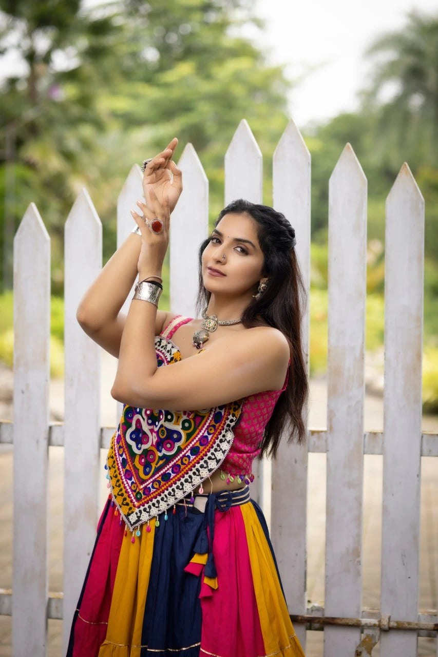 Woman in traditional outfit posing in front of a white picket fence with greenery in the background