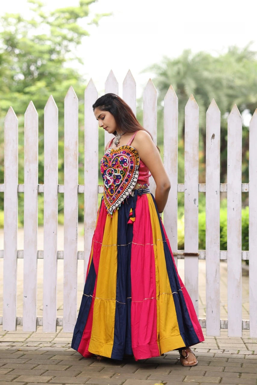 Woman wearing a colorful traditional dress with a white picket fence and greenery in the background