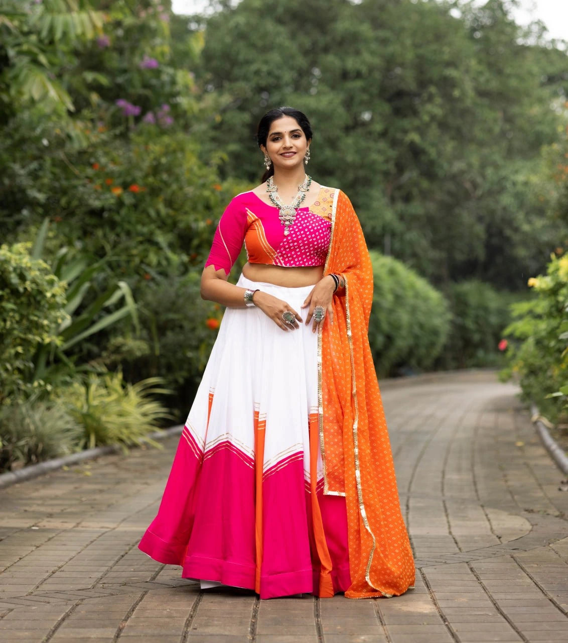 Woman in a colorful traditional outfit standing on a pathway with greenery in the background
