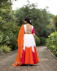 Woman in a traditional outfit with orange and white dress walking on a path surrounded by greenery.