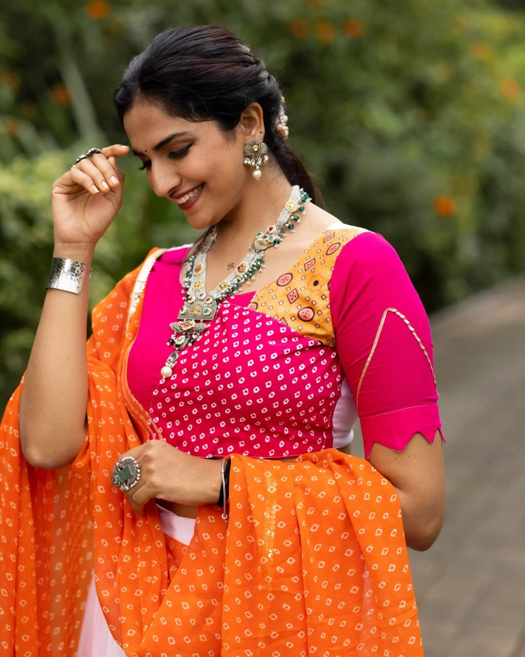 Woman in a traditional orange and pink saree with jewelry against a blurred natural background