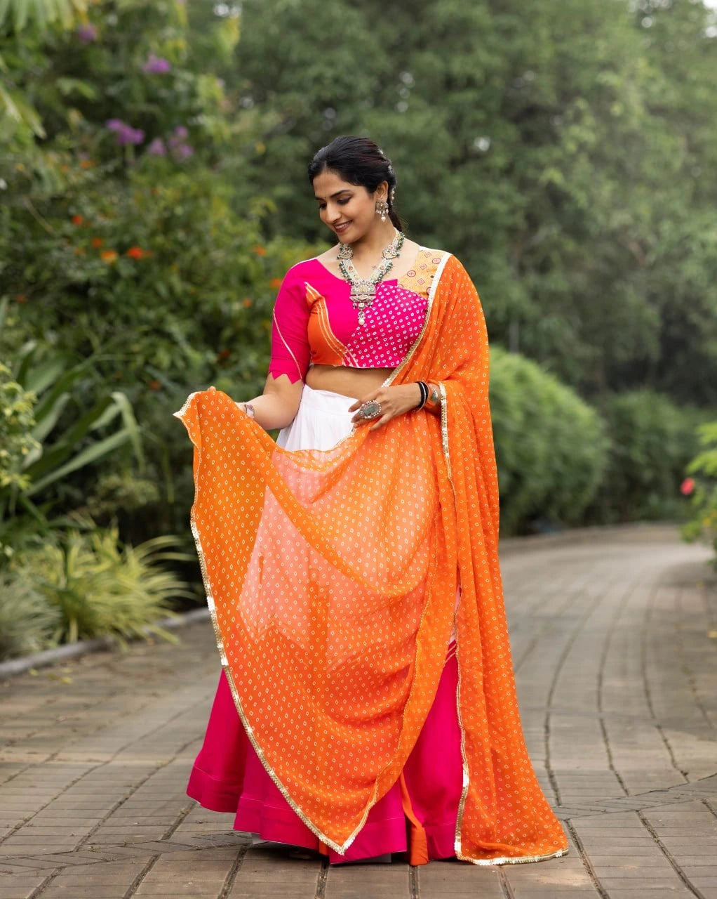 Woman in a pink and orange saree standing outdoors with greenery in the background