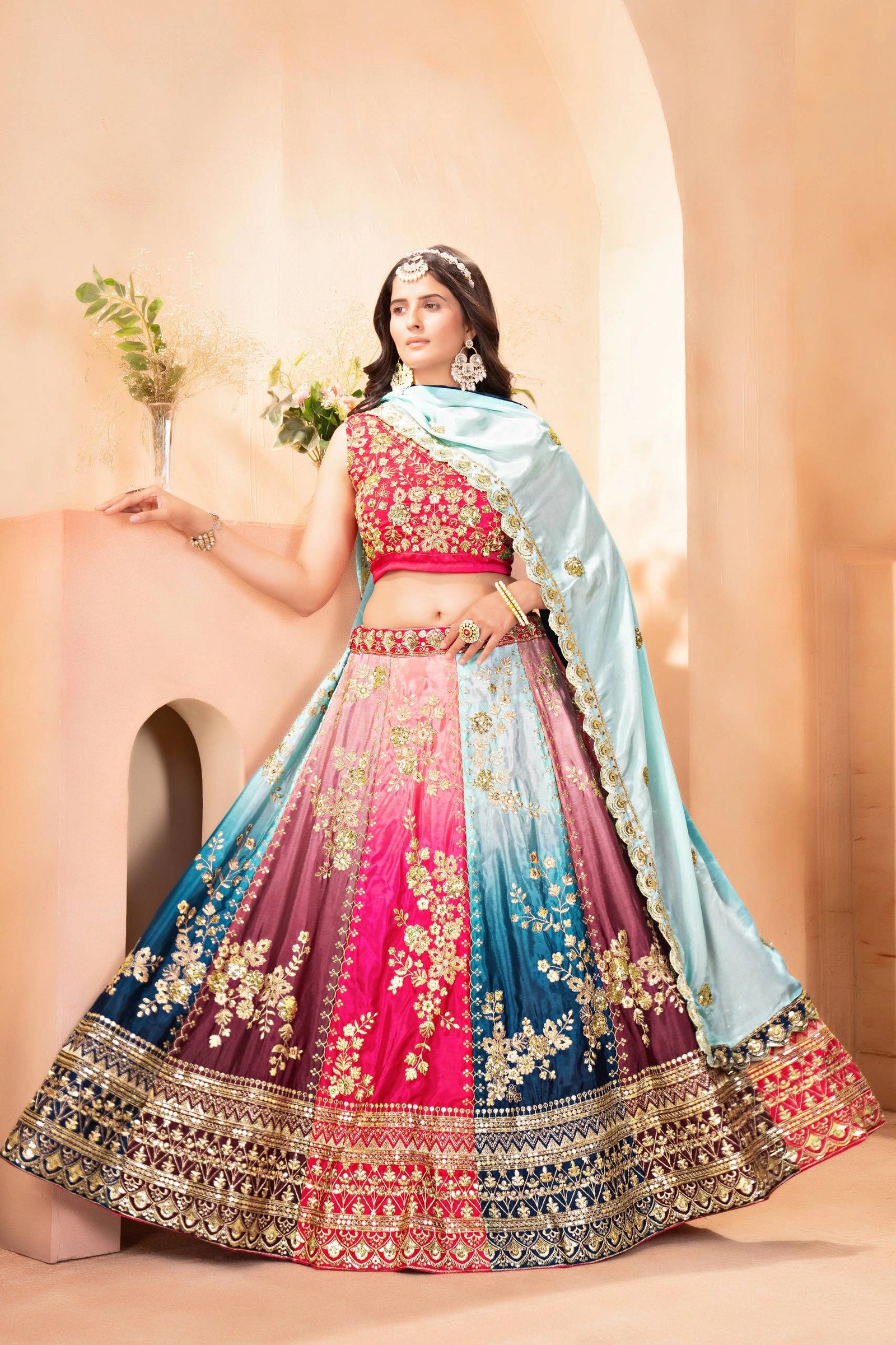 Woman in a colorful traditional outfit with a light blue dupatta against a beige background