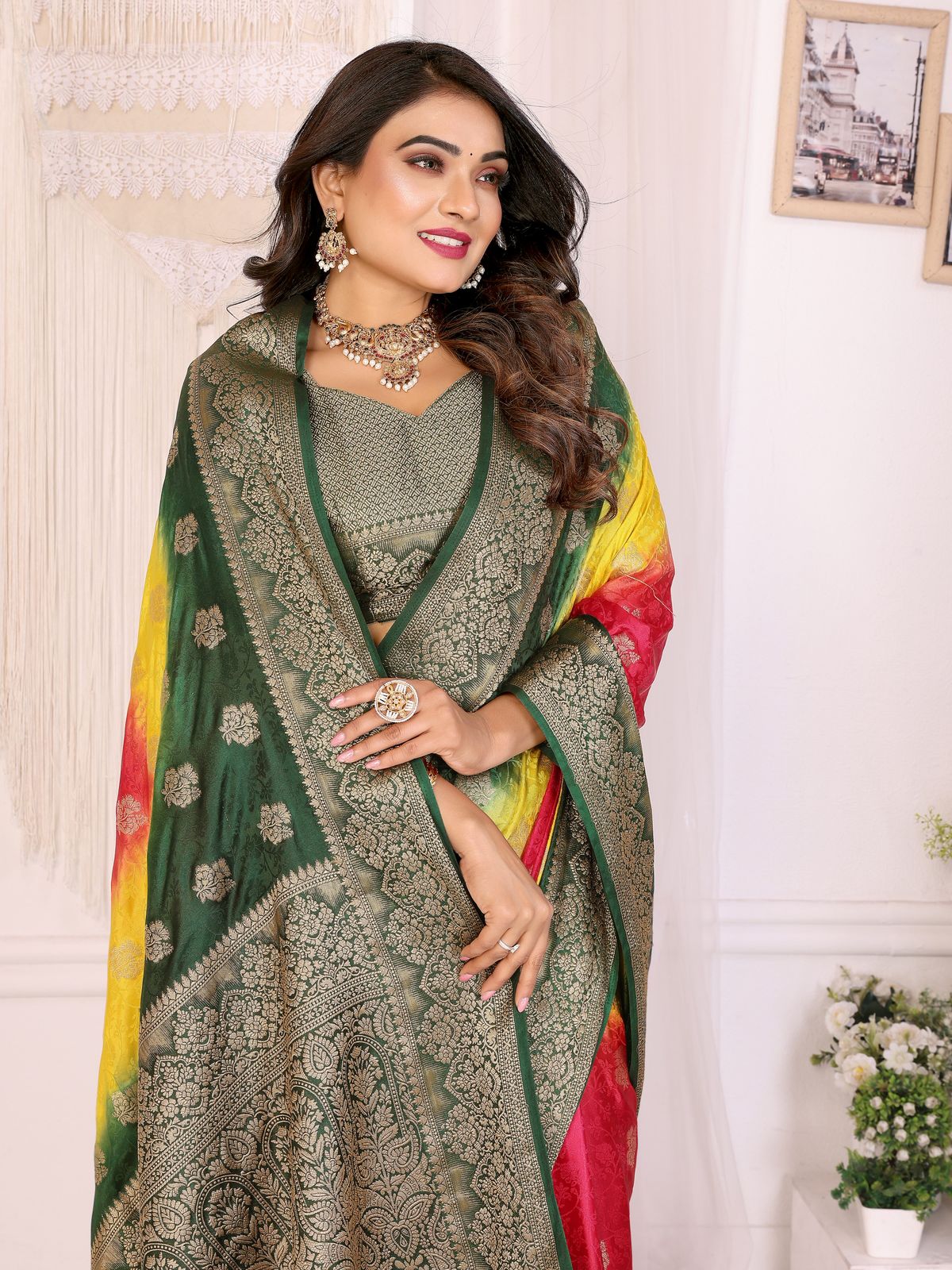 Woman wearing a traditional saree with a green and yellow pattern, standing against a white wall.