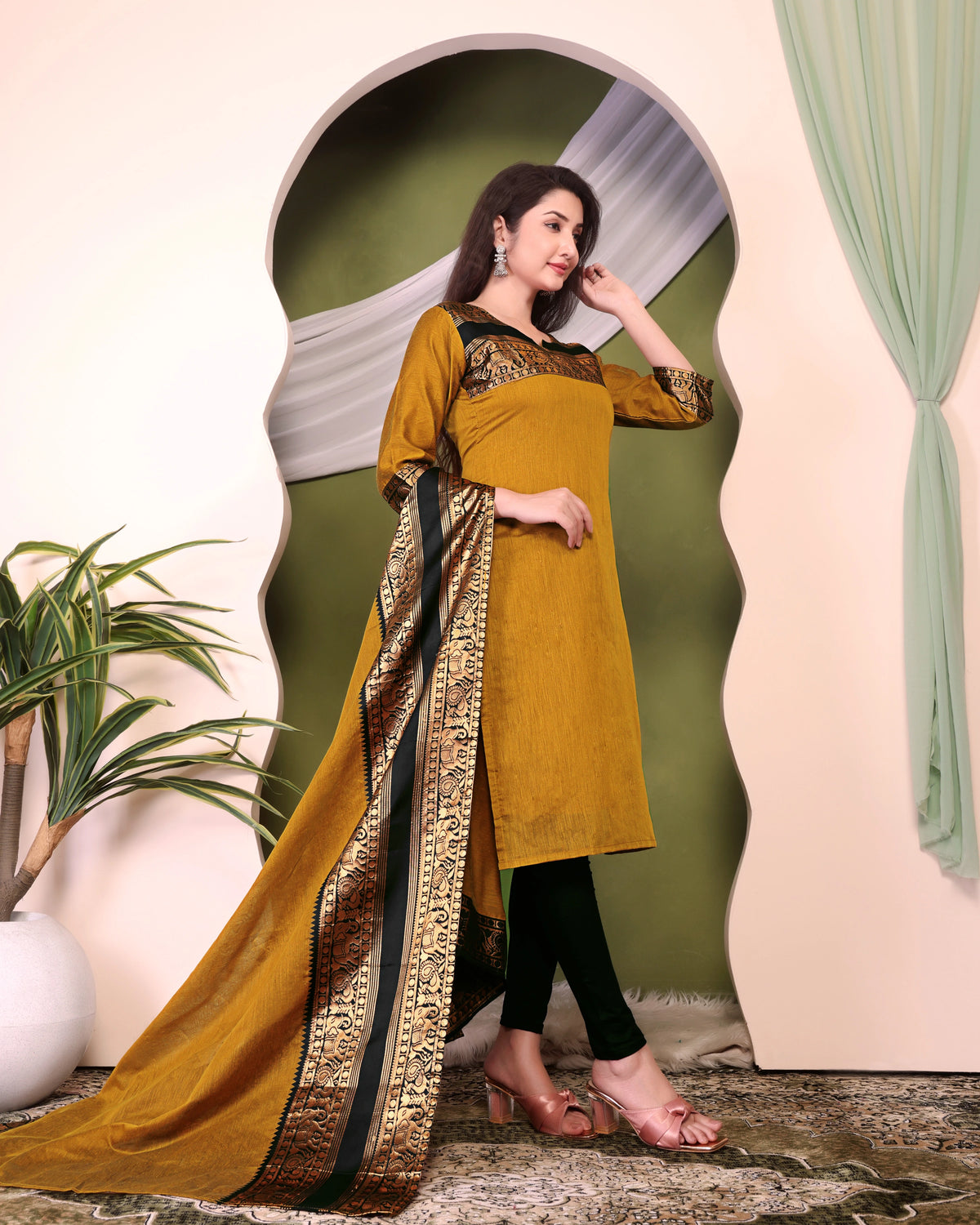 Woman wearing a mustard yellow traditional outfit with a decorative scarf in a stylish setting.