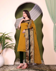 Woman wearing a mustard yellow dress with black and gold details in an indoor setting.