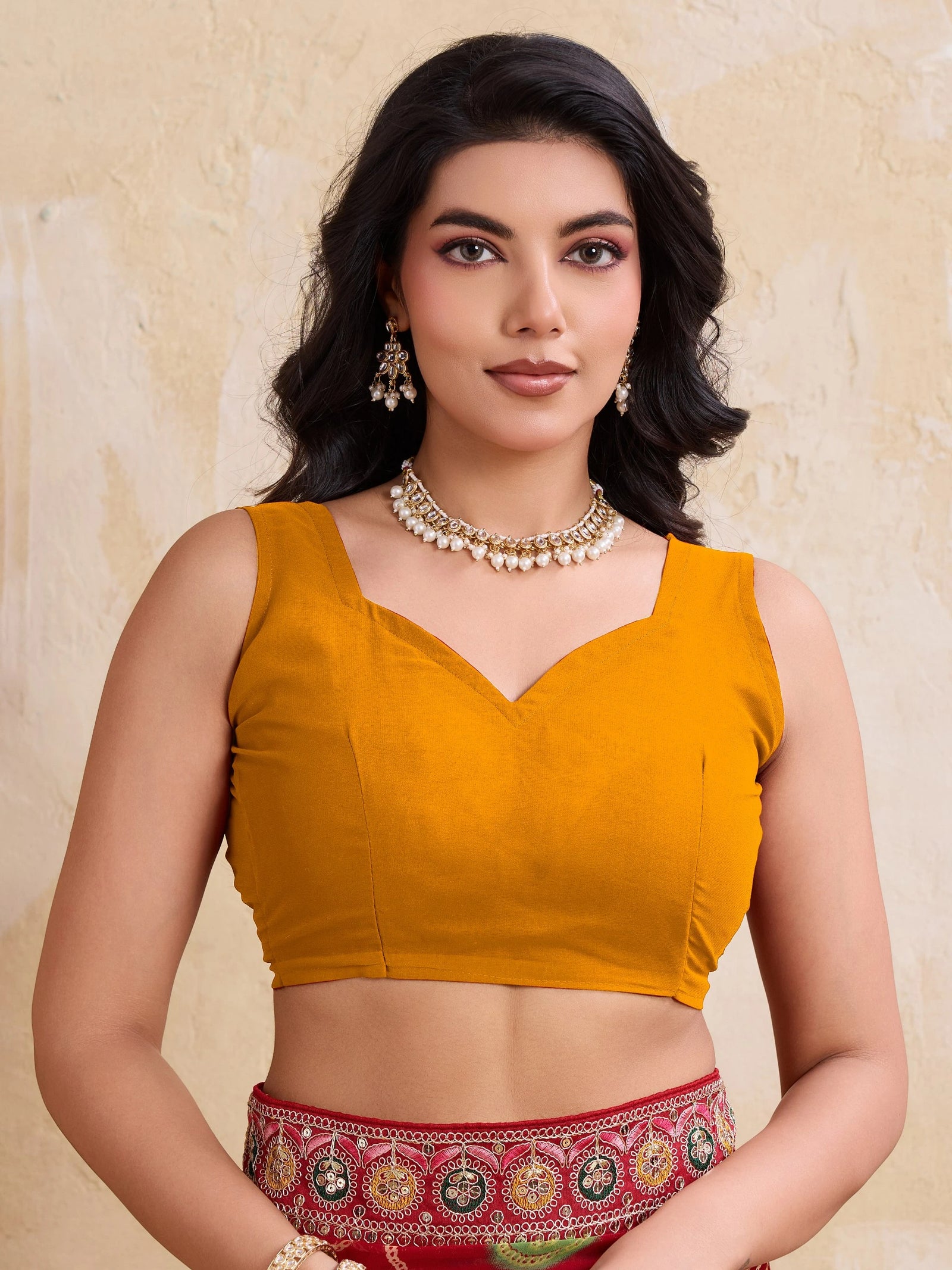 Woman wearing a mustard yellow blouse with a red and gold patterned skirt against a beige background