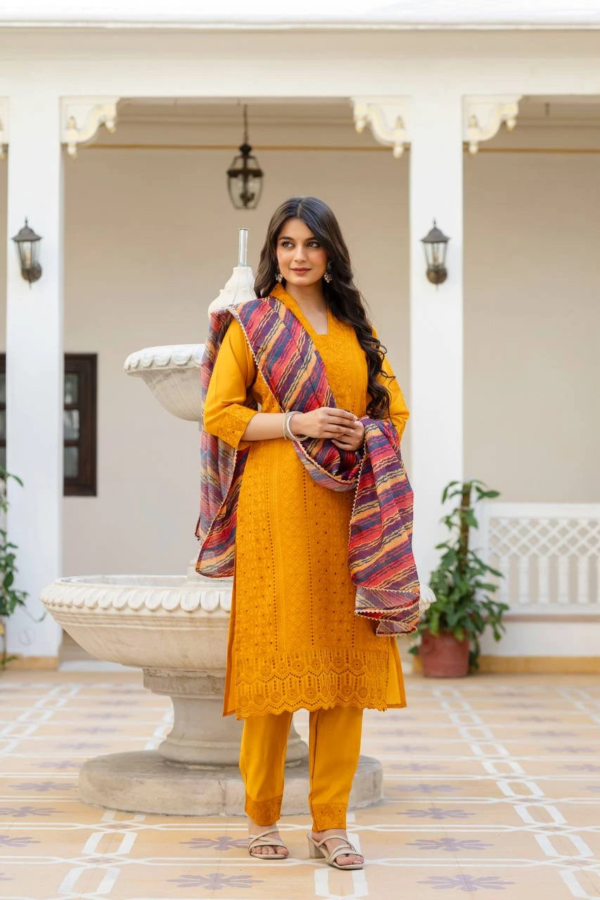 Woman in a mustard yellow traditional outfit with a colorful scarf standing in an outdoor setting.