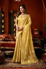 Woman in a yellow saree standing in an ornate room with red walls and decorative elements.