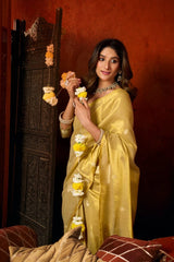 Woman in a yellow saree holding decorative items against a dark red background